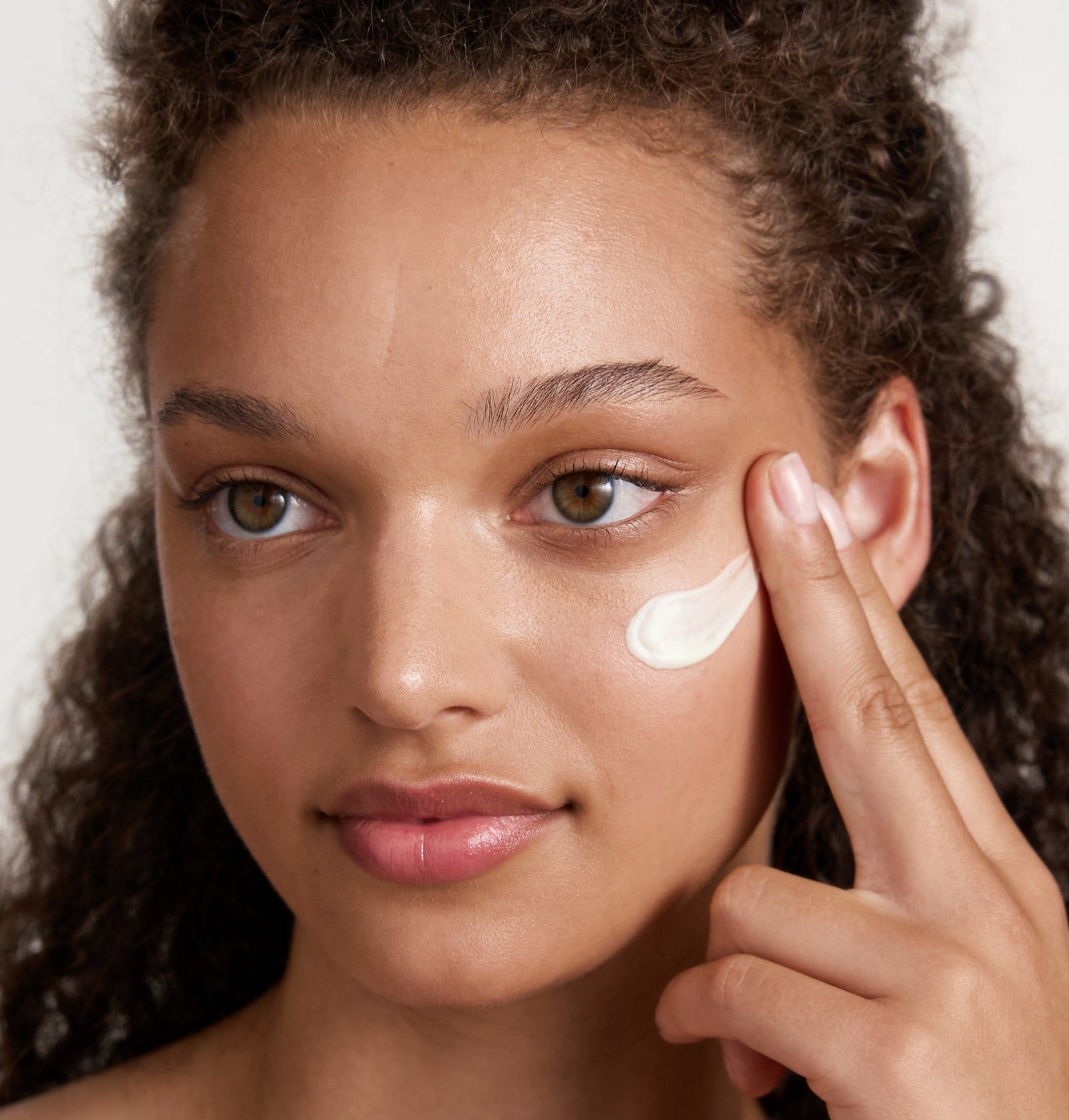 Person trägt Creme auf die Haut auf. Creme ist hell und wird mit dem Finger aufgetragen.