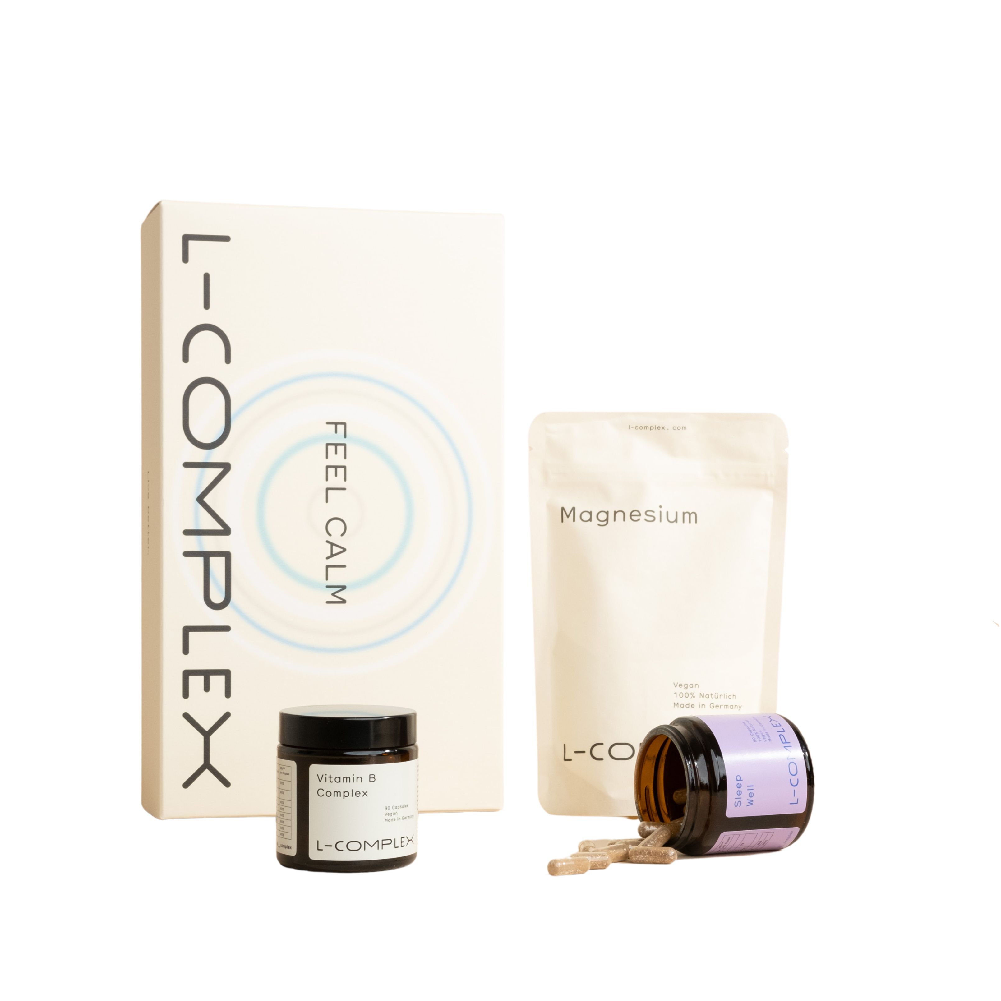 Verschiedene L-Complex Produkte: Karton, Beutel, Gläser. Aufschrift: FEEL CALM, Magnesium, Vitamin B Complex. Kapseln liegen daneben.