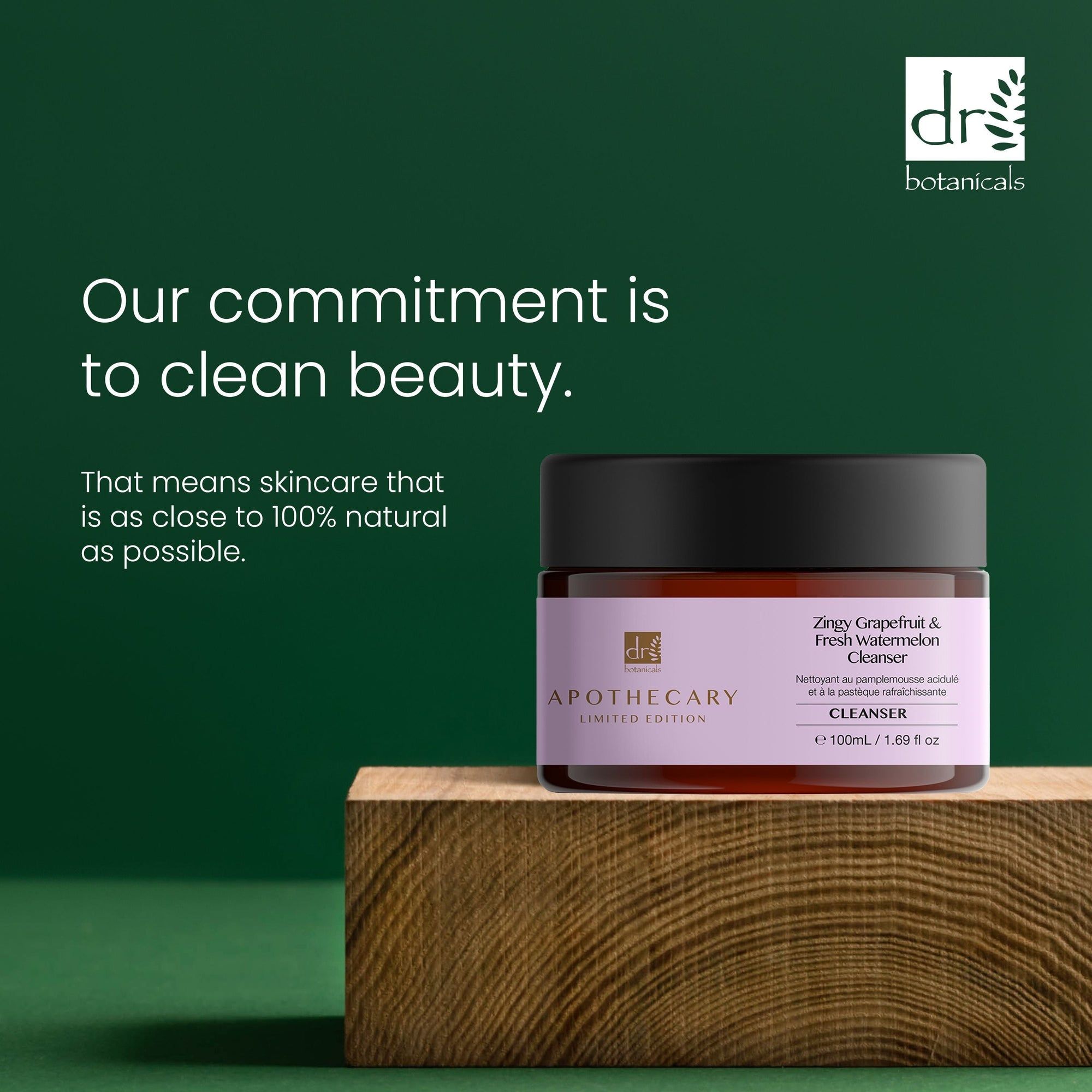 Braunes Glas mit schwarzem Deckel. Etikett mit Produktnamen und Marke. Text: Our commitment is to clean beauty. Auf Holzblock.