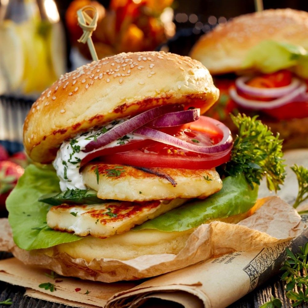 Burger mit Grillkäse, Tomate, Zwiebeln und Salat. Auf einem Brötchen mit Sesam. Auf braunem Papier.