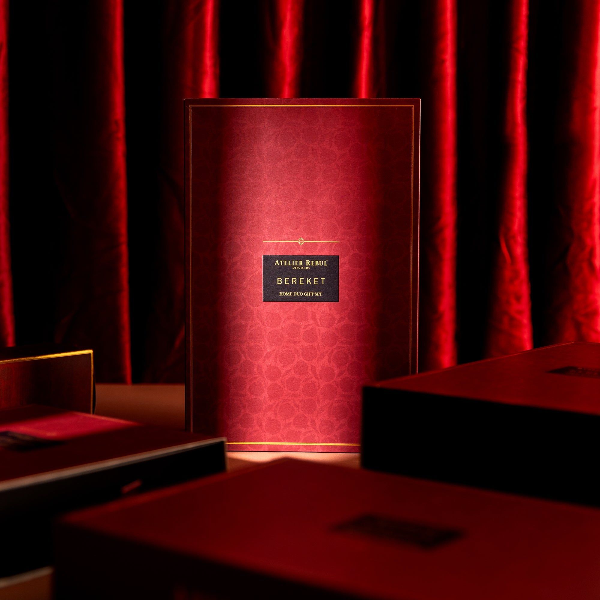 Burgunderrote Geschenkbox mit goldfarbenem Rahmen. Aufschrift: Atelier Rebul Bereket. Mehrere weitere Boxen im Hintergrund.