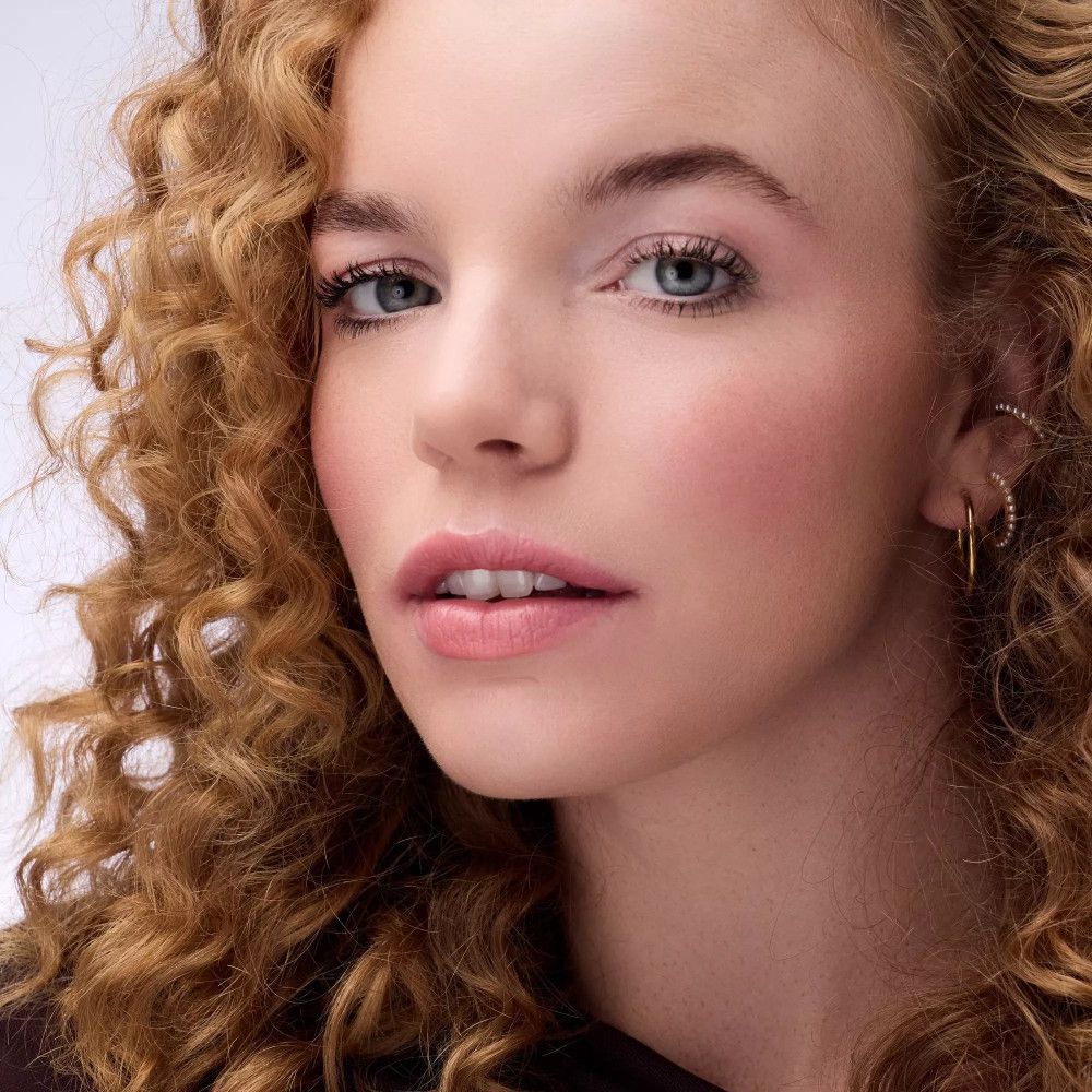 Porträt einer Frau mit rosa Rouge auf den Wangen. Sie trägt goldene Ohrringe.