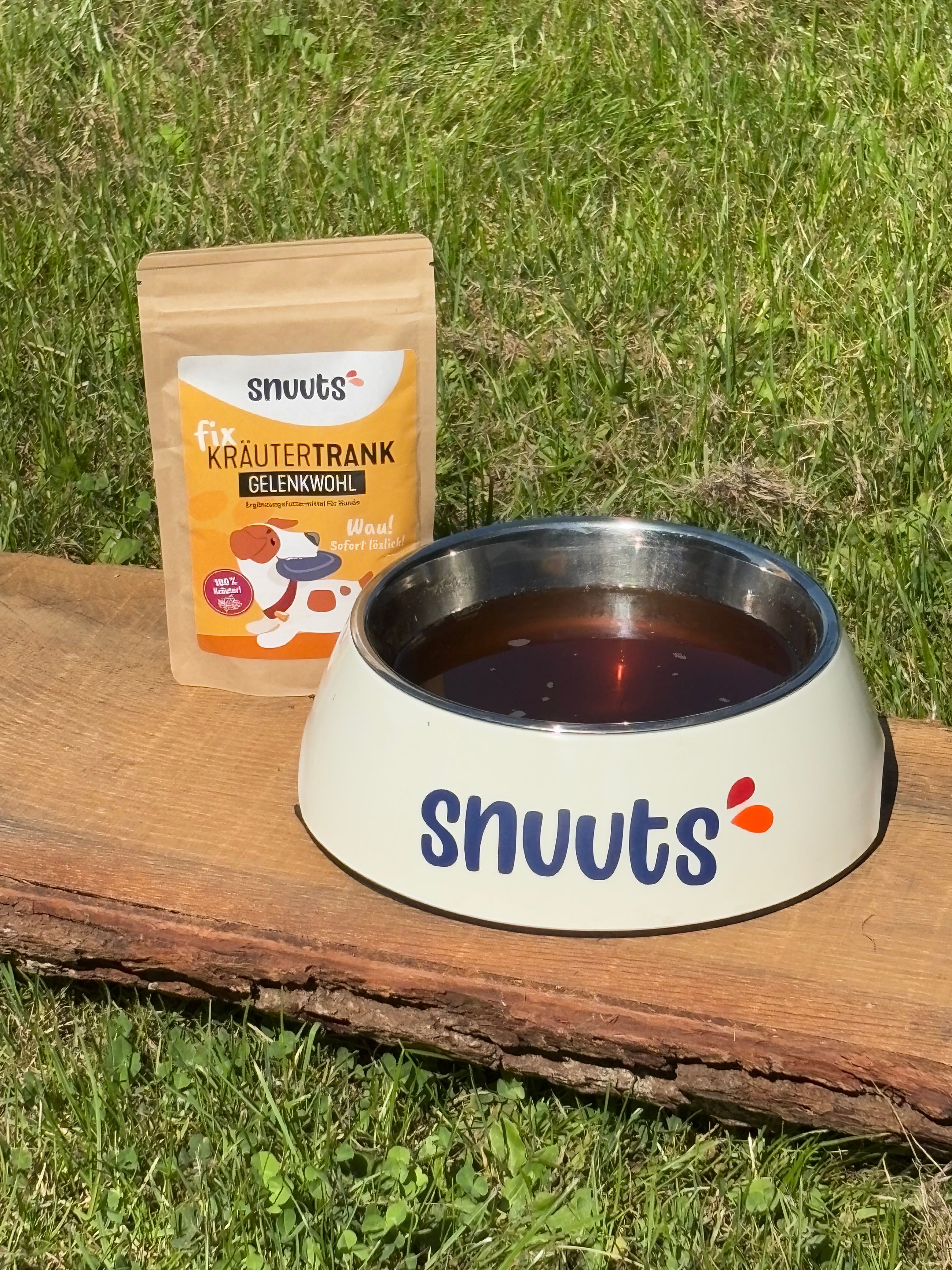 Produktbeutel neben einer Futterschüssel. Futterschüssel mit Flüssigkeit. Aufdruck auf Beutel: "snuuts Kräutertrank Gelenkwohl". Aufdruck auf Schüssel: "snuuts".