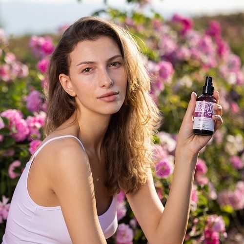 Frau hält eine Sprühflasche vor Rosenblüten. Aufschrift: Alteya Organics, Rose Water. USDA Organic-Zertifizierung.