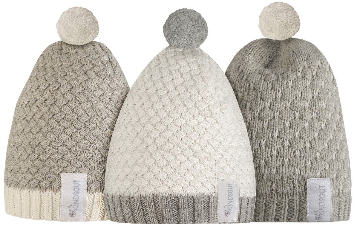 Drei grau-weiße Bommelmützen nebeneinander. Strickmuster, Bommel oben. Label mit Kindsgut-Logo.