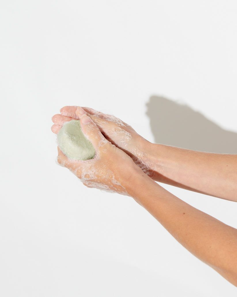 Hände halten einen grünen, runden Shampoo-Block. Schaum. Auf weißem Hintergrund.