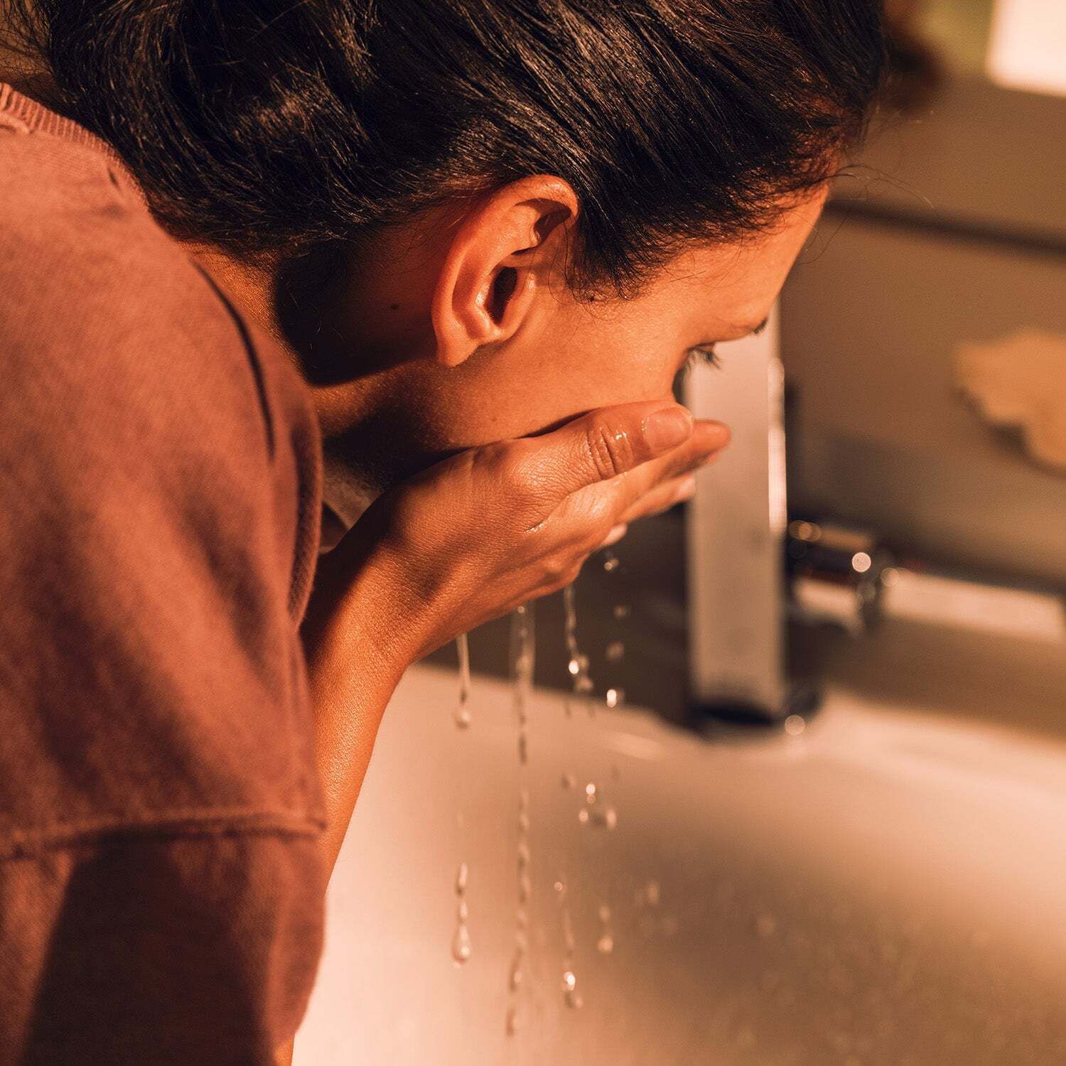 Frau wäscht ihr Gesicht am Waschbecken. Nahaufnahme, Profilansicht. Wasser fließt.