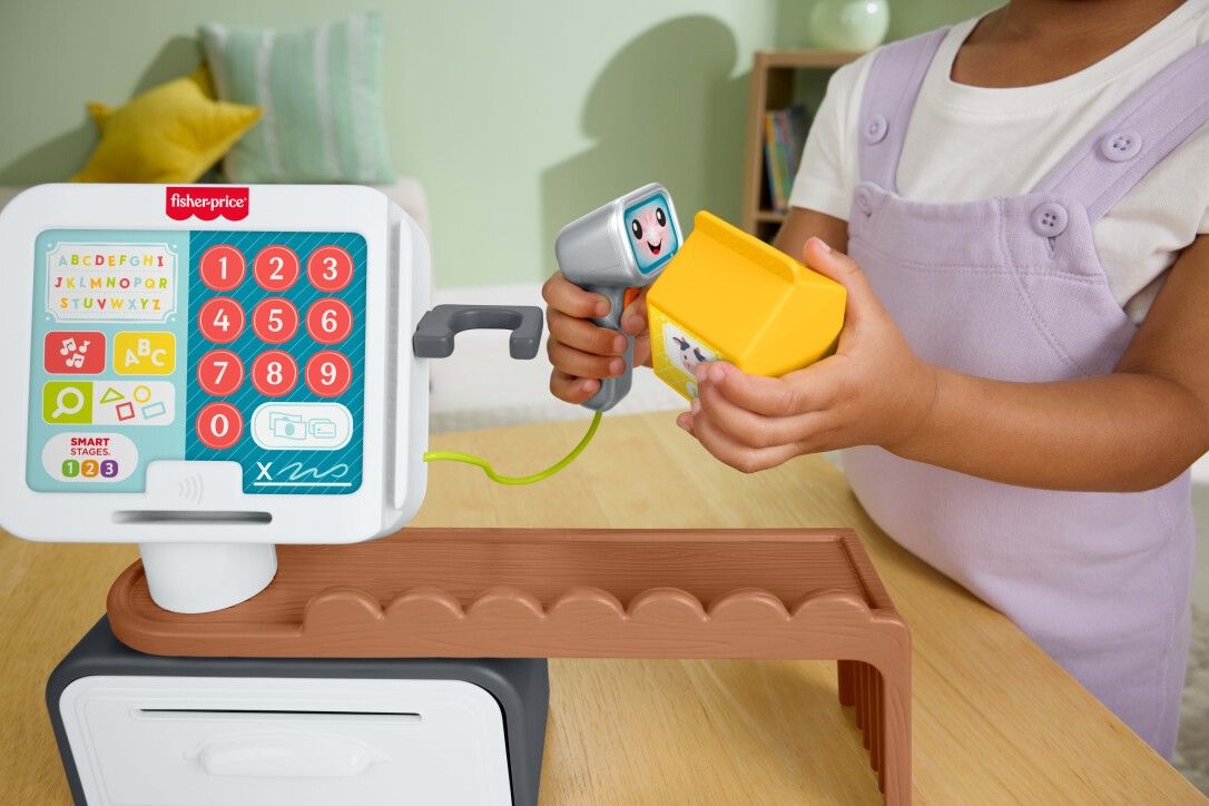 Kind spielt mit Spielzeugkasse. Scanner und gelbes Produkt in der Hand. Fisher-Price Logo.