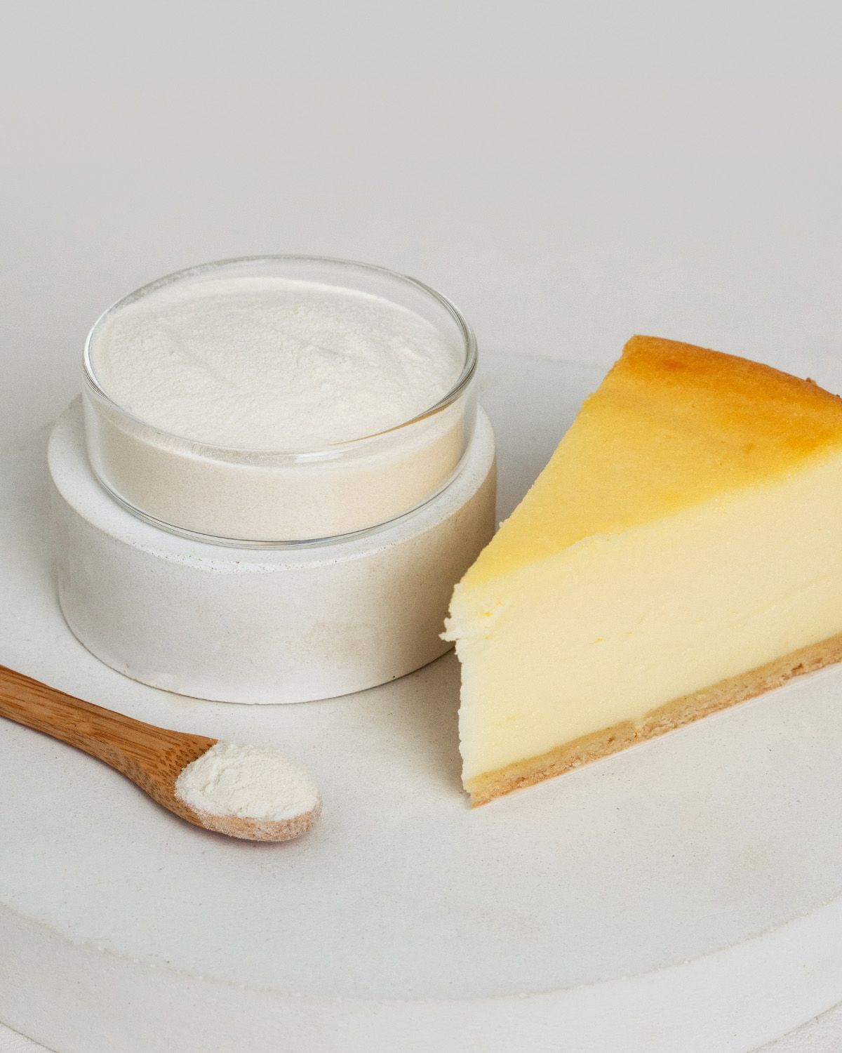 Xanthan Gum Pulver in einem Glasbehälter neben einem Stück Käsekuchen und einem Löffel.
