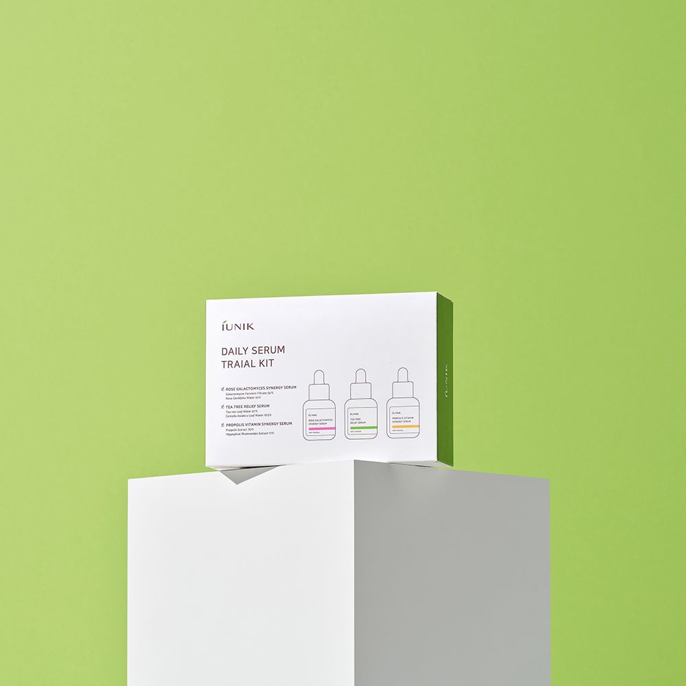 Weiße Verpackung mit drei Serumflaschen auf einem weißen Podest vor grünem Hintergrund. Auf der Verpackung steht "IUNIK DAILY SERUM TRIAL KIT".