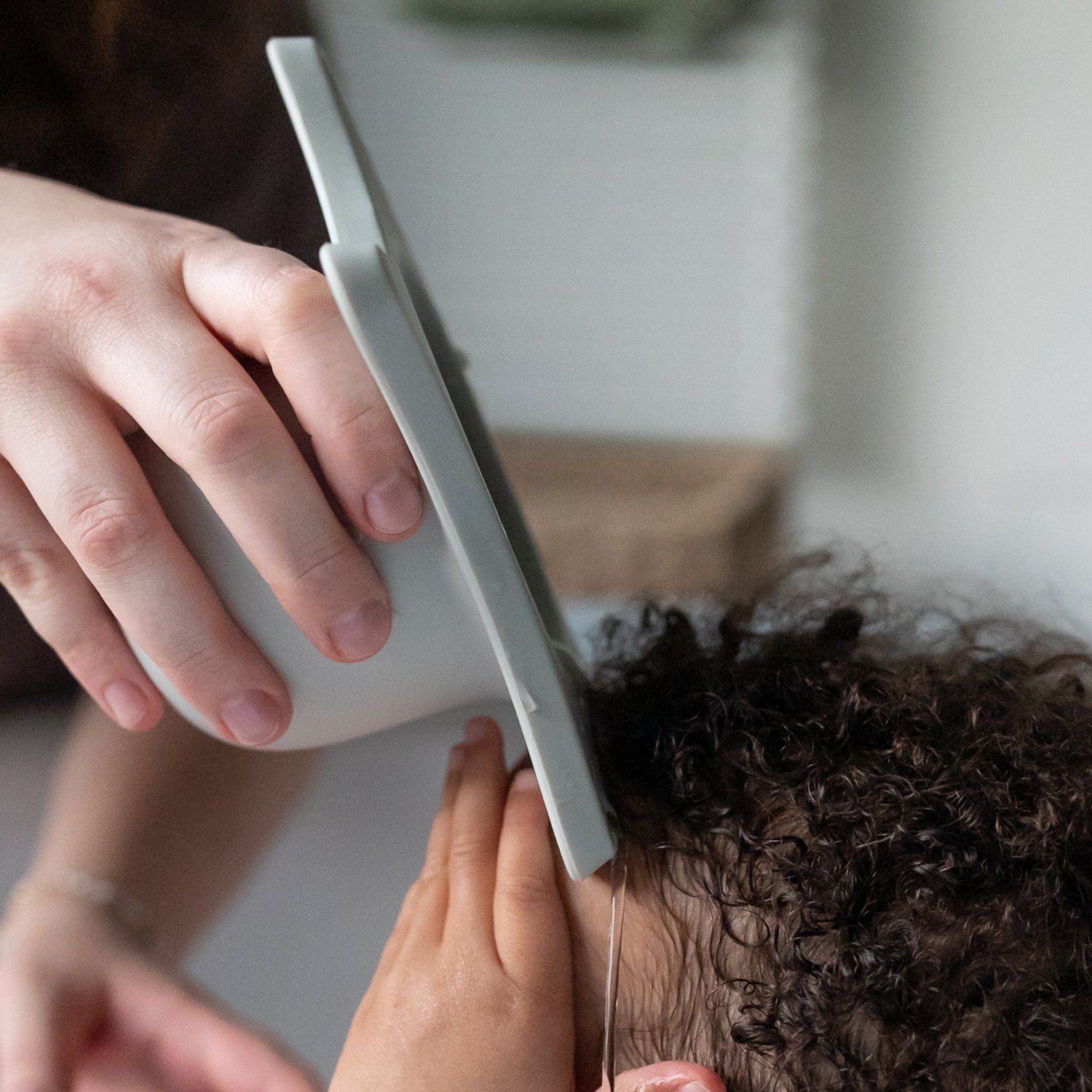 Person hält hellgraue Duschhilfe über dem Kopf eines Kindes. Das Kind hat lockiges Haar. Nahaufnahme.