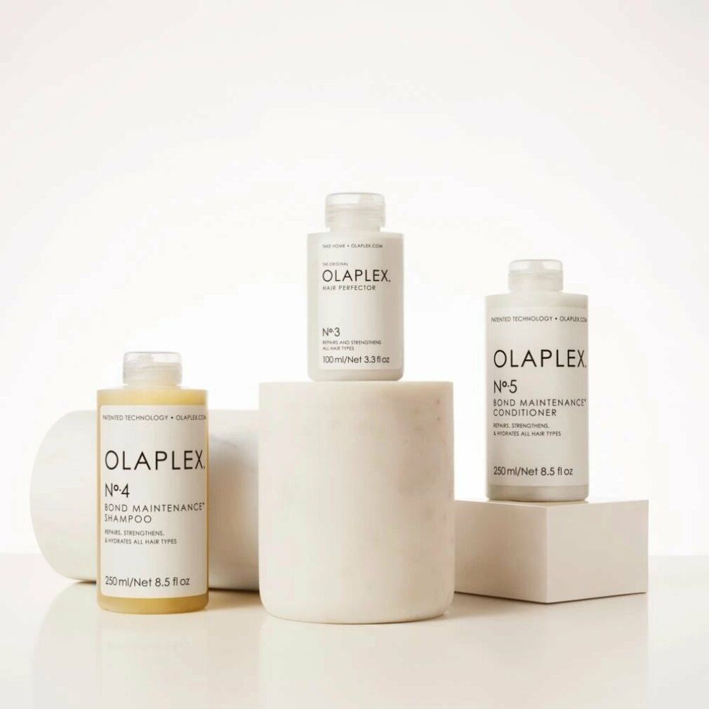 Drei Olaplex-Produkte: Nº4, Nº3 und Nº5 Bond Maintenance Conditioner. Auf weißen Podesten. Enthält 250 ml/8,5 fl oz. Repariert, stärkt und hydratisiert.