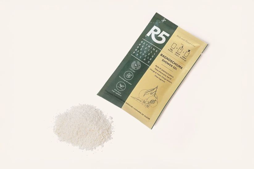Duschgel-Beutel und Pulver. Grün-beige Verpackung mit Text: R5, Bagnoschiuma, Orange & Pfirsich. Made in Italy.