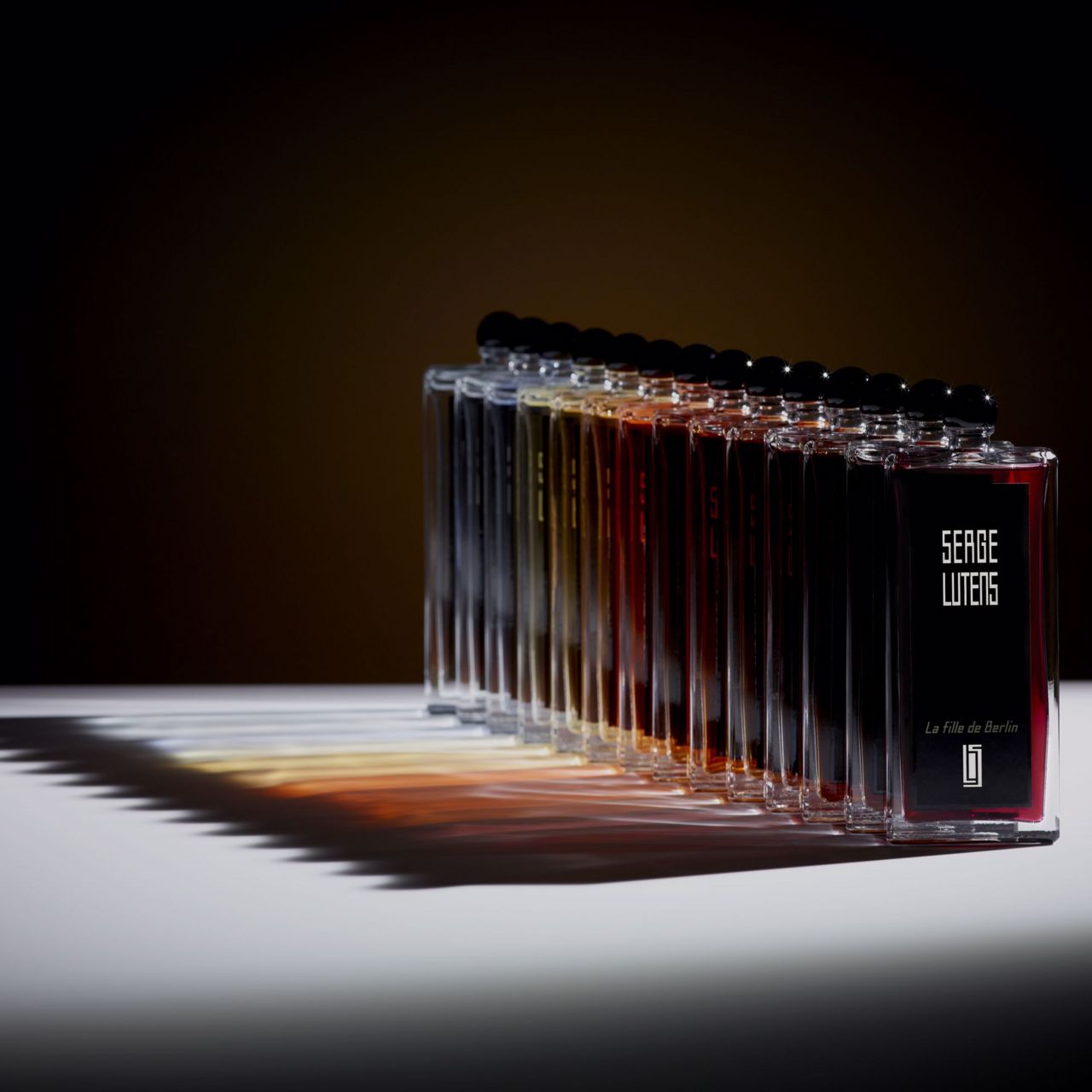 Reihe von Flakons mit schwarzem Verschluss. Schwarze Etiketten mit weißem Schriftzug. Produktname und Marke sichtbar.