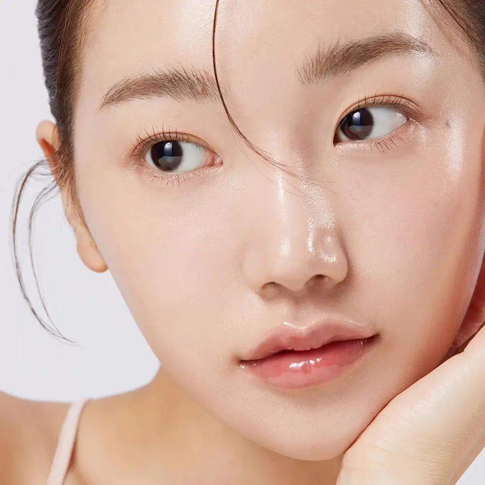 Nahaufnahme einer Frau mit glänzender Haut. Sie stützt ihr Kinn mit der Hand.