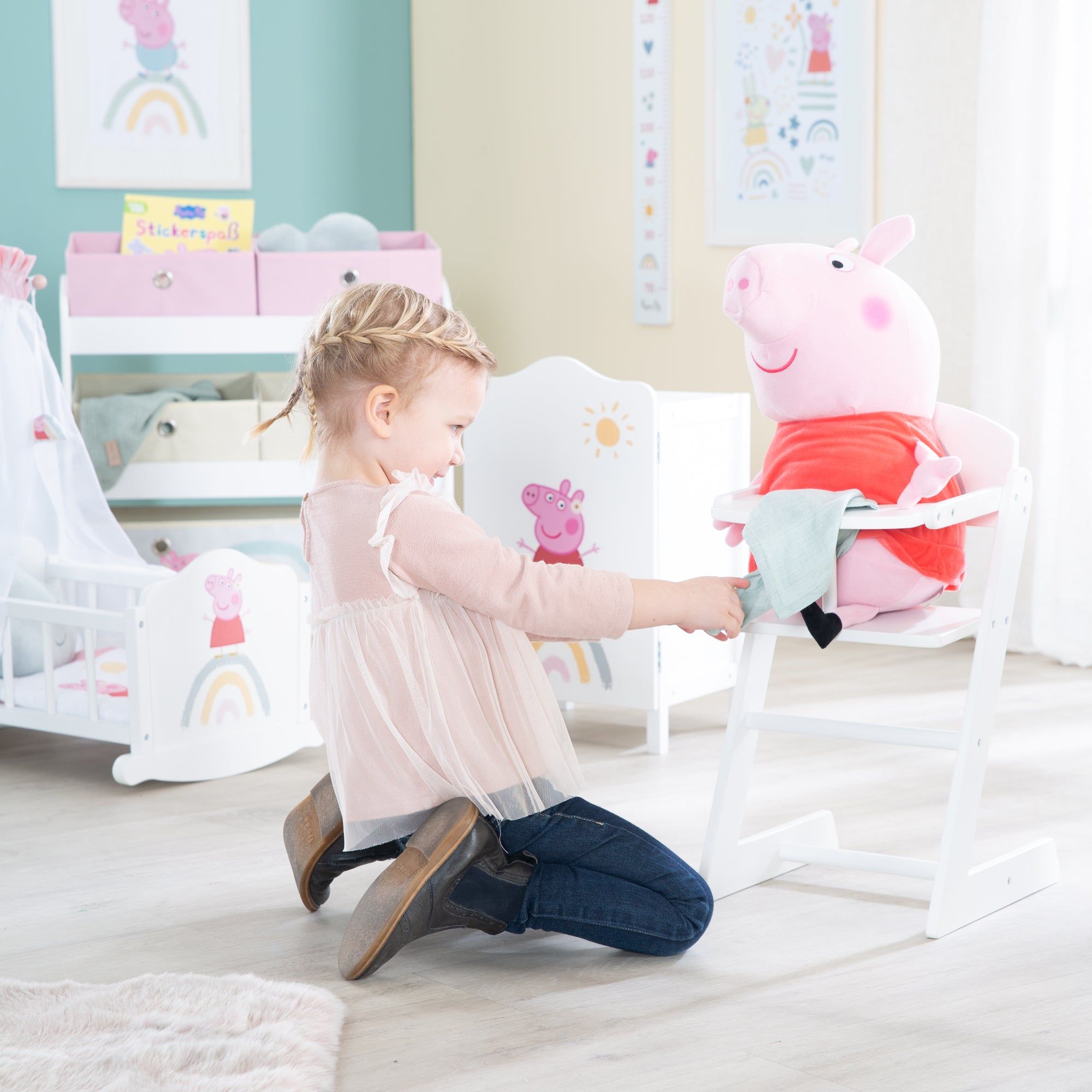 Weißer Puppenhochstuhl mit Peppa Pig-Motiv. Ein Kind sitzt vor dem Stuhl. Im Hintergrund weitere Kindermöbel.