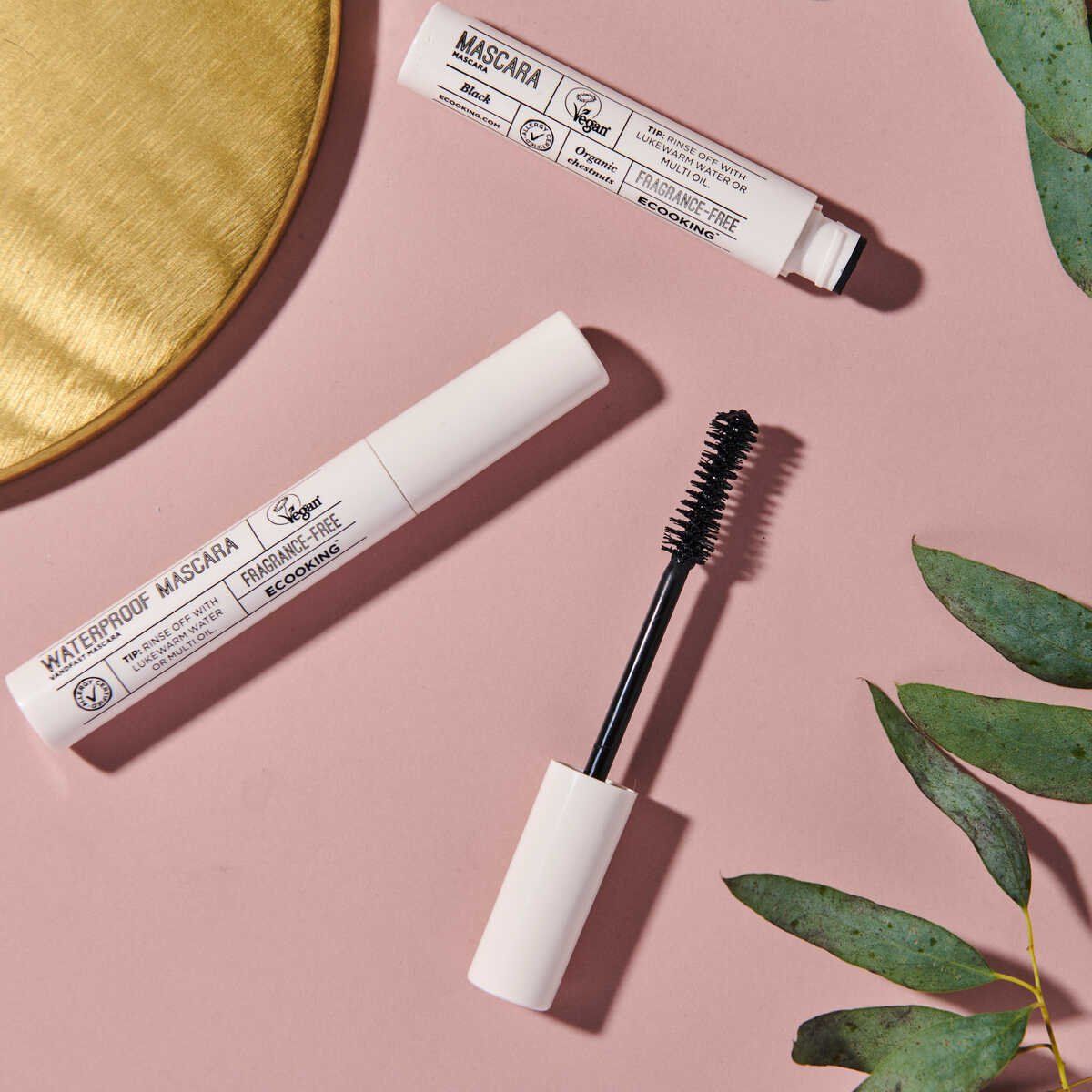 Mascara-Tuben und Bürste auf rosa Oberfläche. Weiße Deckel, schwarze Bürsten. Vegan-Logo und Text: „WATERPROOF MASCARA“ und „FRAGRANCE-FREE“.