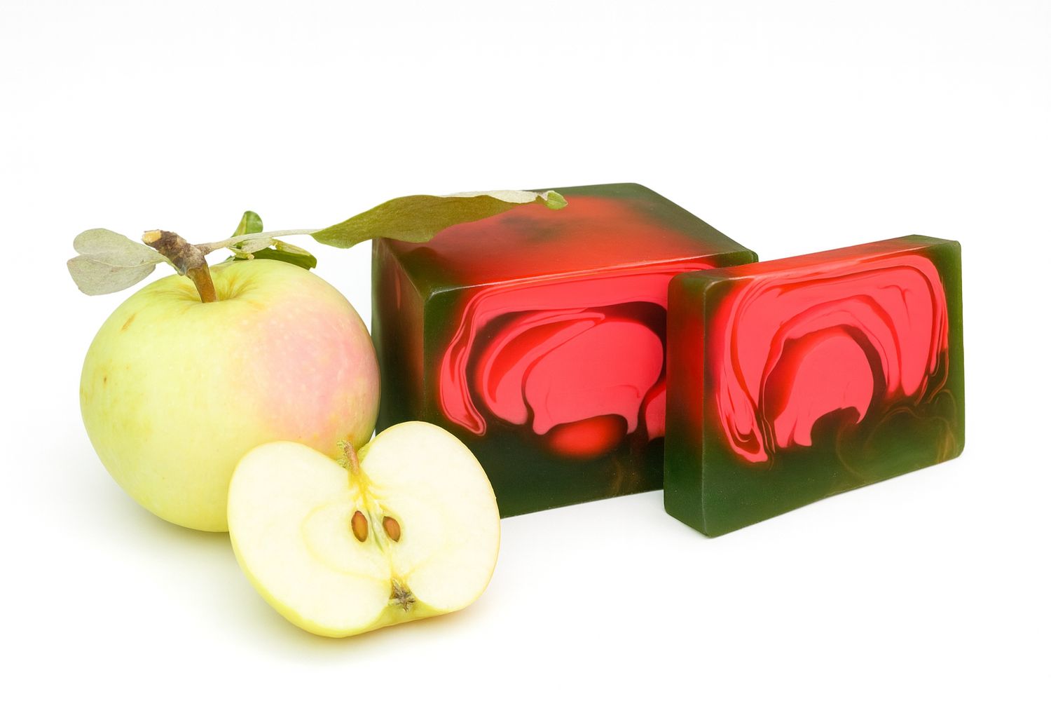 Grüner Apfel und Seifenstücke mit rotem Muster. Ein Apfel ist halbiert. Die Seife hat eine grüne Basis und rotes Muster.