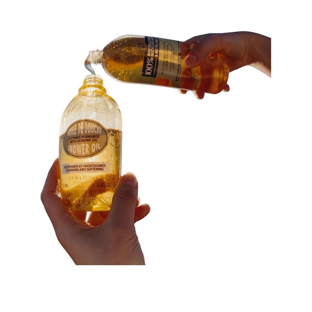 Hände gießen Mandel Duschöl aus einer Flasche in eine kleinere Flasche. Etikett sichtbar.