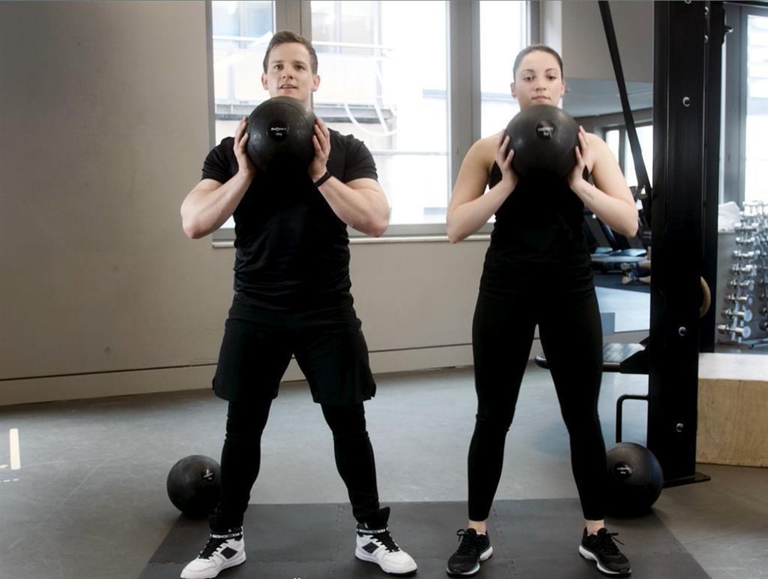 Zwei Personen halten jeweils einen schwarzen Slamball. Fitnessstudio-Umgebung.