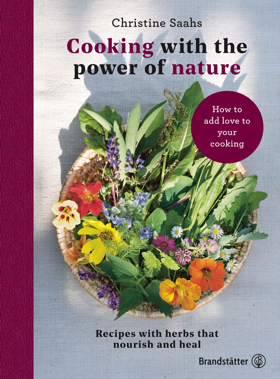 Buchcover: "Cooking with the power of nature". Kräuter und Blumen in einem Korb. Autorin: Christine Saahs.