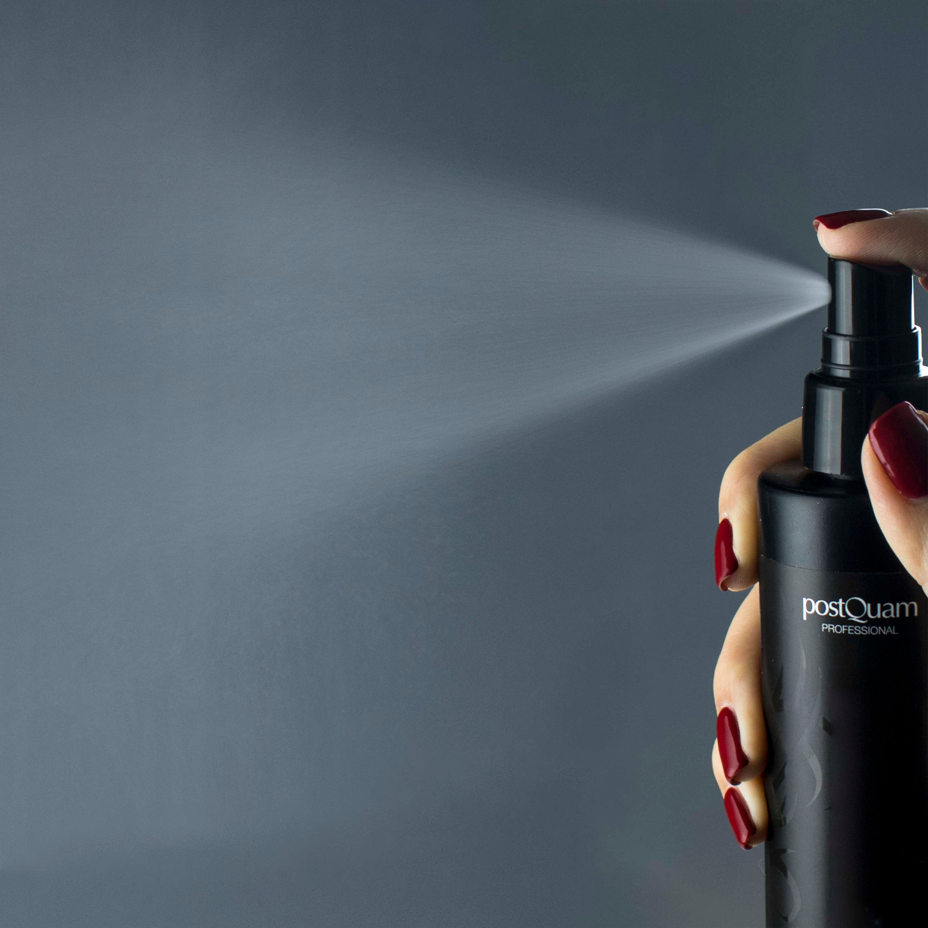 Schwarze Sprühflasche in einer Hand. Sprühnebel sichtbar. Marke: PostQuam Professional.