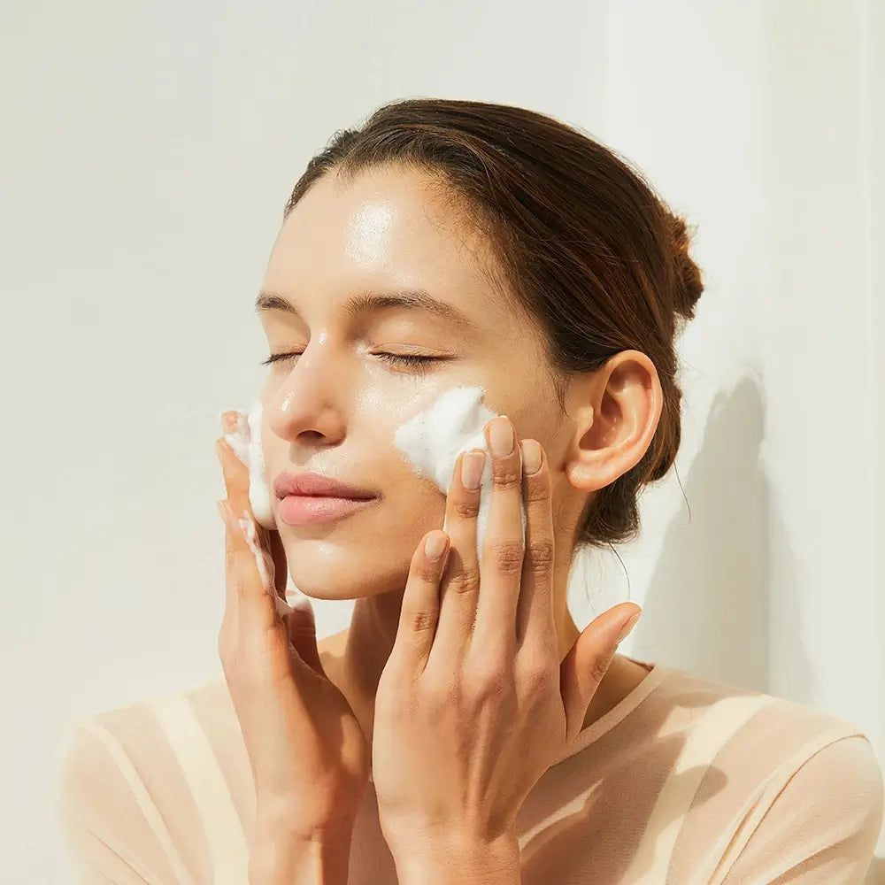 Frau wäscht ihr Gesicht mit Schaum. Augen geschlossen. Hände am Gesicht.