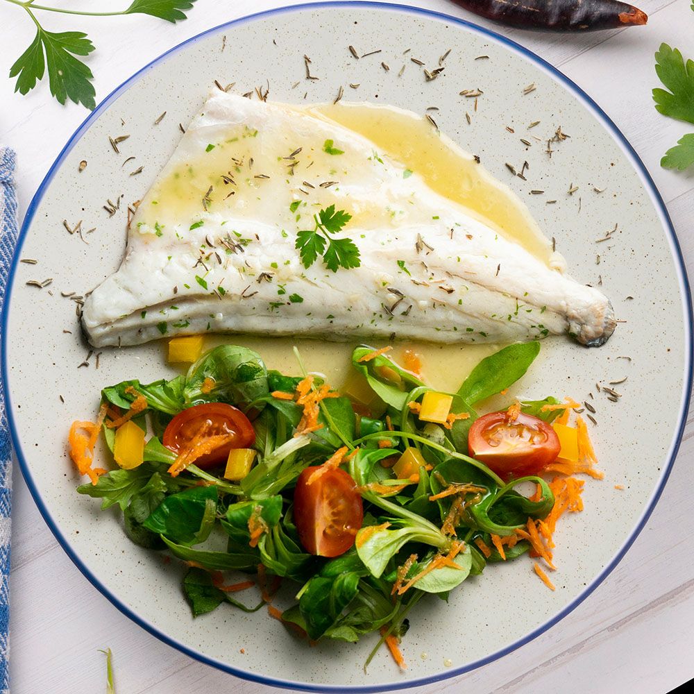 Teller mit Fischfilet, Salat und Tomaten. Fisch mit Soße. Salat mit Karotten und Tomaten. Dekoration mit Kräutern.