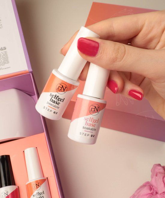 Zwei Flaschen mit weißem Deckel. Aufschrift: selfgel base soakable, STEP 02. PN-Logo. In Hand gehalten.