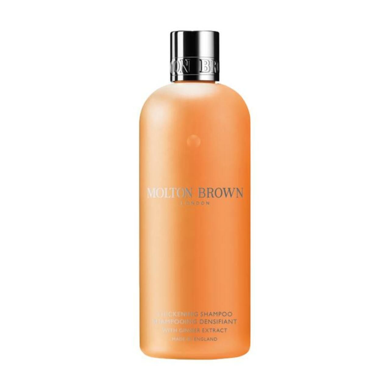 Orangefarbene Shampoo-Flasche mit silbernem Deckel. Aufschrift: Molton Brown London. Produktbezeichnung: Thickening Shampoo mit Ingwer Extrakt.