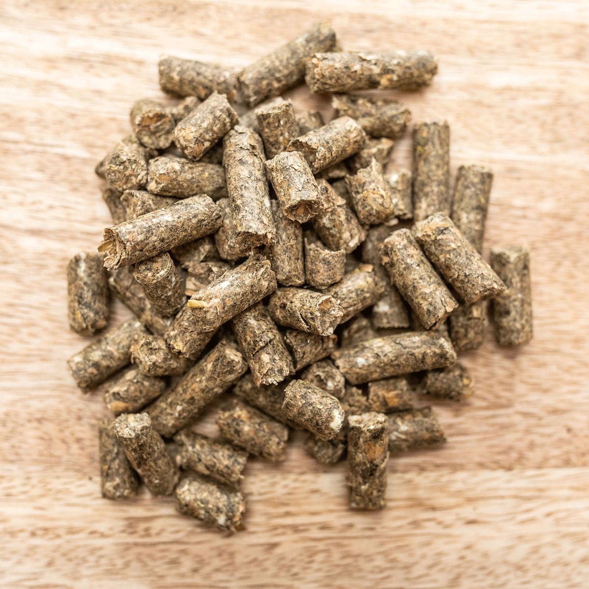 Haufen zylindrischer Pellets auf Holzbrett. Braune Farbe, raue Textur. Draufsicht.