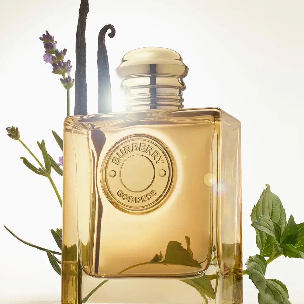 Goldfarbener Flakon mit goldfarbenem Verschluss, umgeben von Pflanzen. Aufschrift Burberry Goddess.