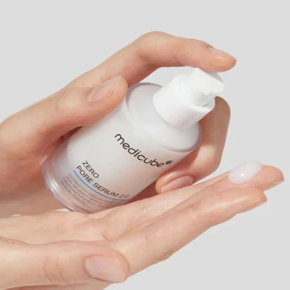 Hände halten eine Flasche MEDICUBE Zero Pore Serum 2.0. Ein Tropfen Serum auf der Handfläche. Aufschrift: medicube, Zero Pore Serum 2.0.