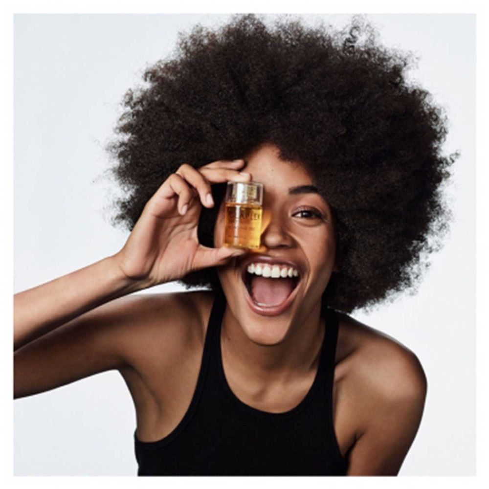 Frau hält Olaplex No.7 Bonding Öl vor ihrem Auge. Sie lächelt. Aufschrift: Olaplex No.7 Bonding Oil.