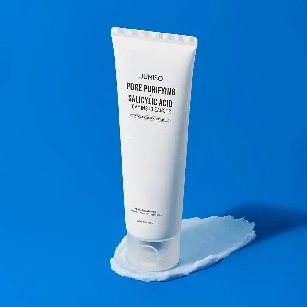 Weiße Tube mit Schaum. Text: JUMISO Pore Purifying Salicylic Acid Foaming Cleanser. Auf blauem Untergrund.