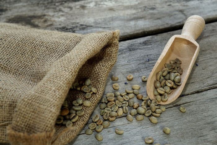 Jutesack mit Kaffeebohnen und Holzschaufel mit Bohnen auf Holzoberfläche. Grüne Kaffeebohnen.