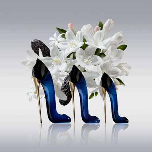 Drei schwarze Flakons in Stöckelschuhform mit goldenem Absatz. Blaue Flüssigkeit sichtbar. Weiße Blüten im Hintergrund.
