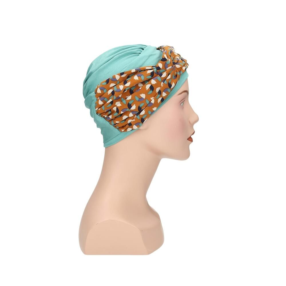 Türkisfarbener Turban mit gemustertem Stirnband auf einer Schaufensterpuppe. Das Stirnband hat ein Muster aus Braun-, Blau- und Beigetönen. Seitenansicht.