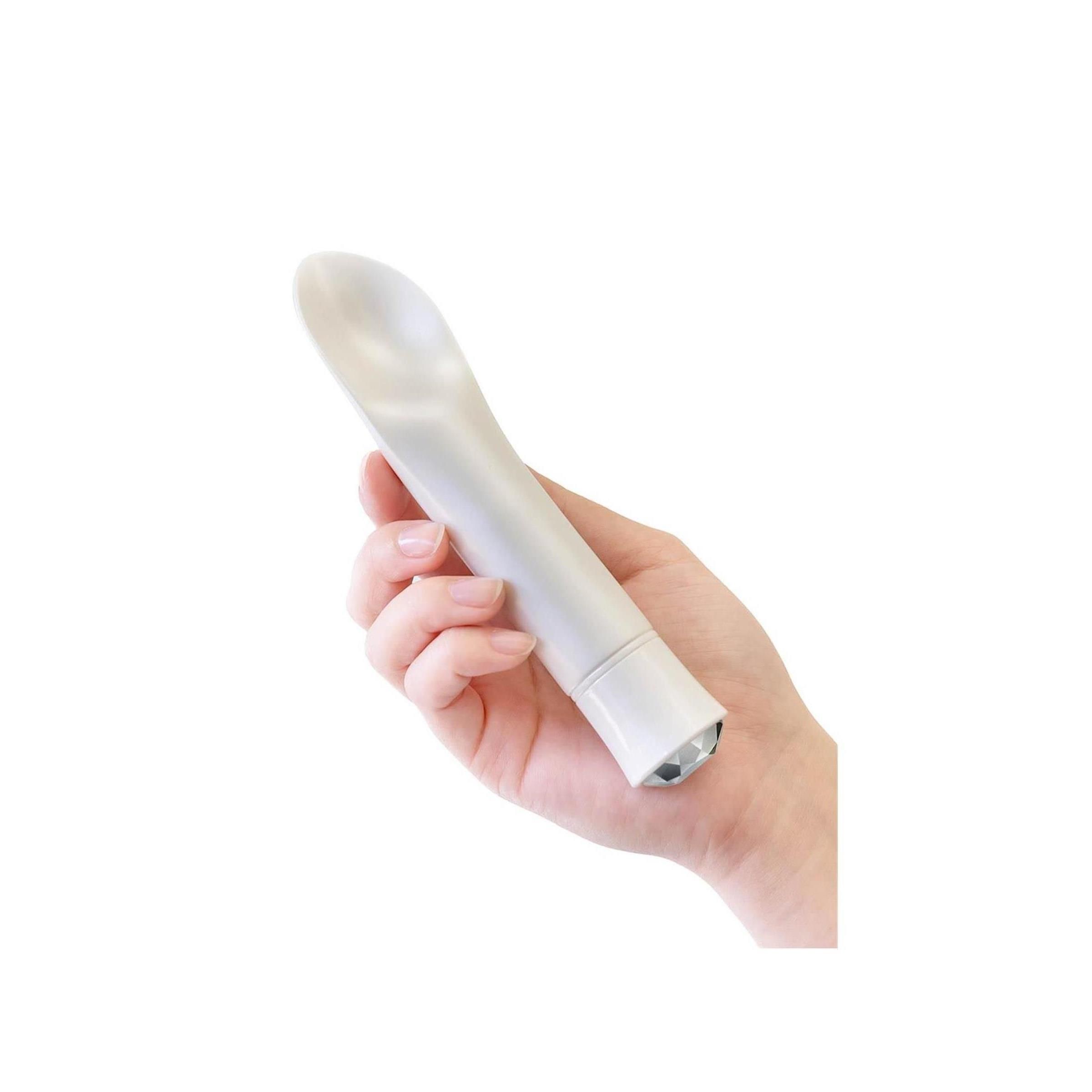 Weißes Wellness-Produkt in einer Hand gehalten. Abgerundeter Kopf, Kristall-Ende.