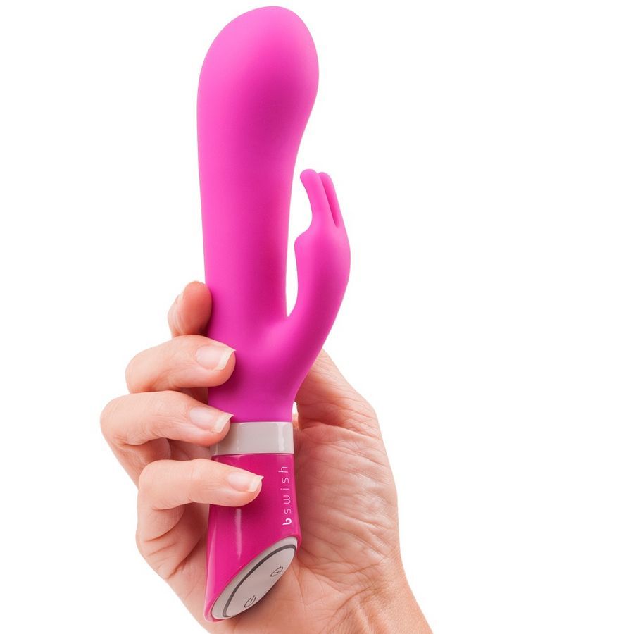 Rosa Vibrator, gehalten. Mit gebogener Form und einem zusätzlichen Element. Marke 'b swish'.