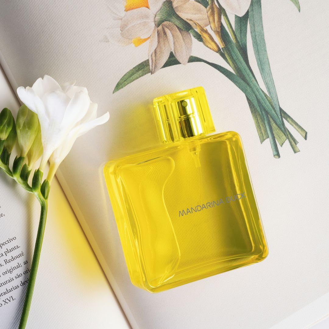 Gelbes Eau de Toilette Spray. Flasche auf Buch mit Blumen. Schriftzug Mandarina Duck.