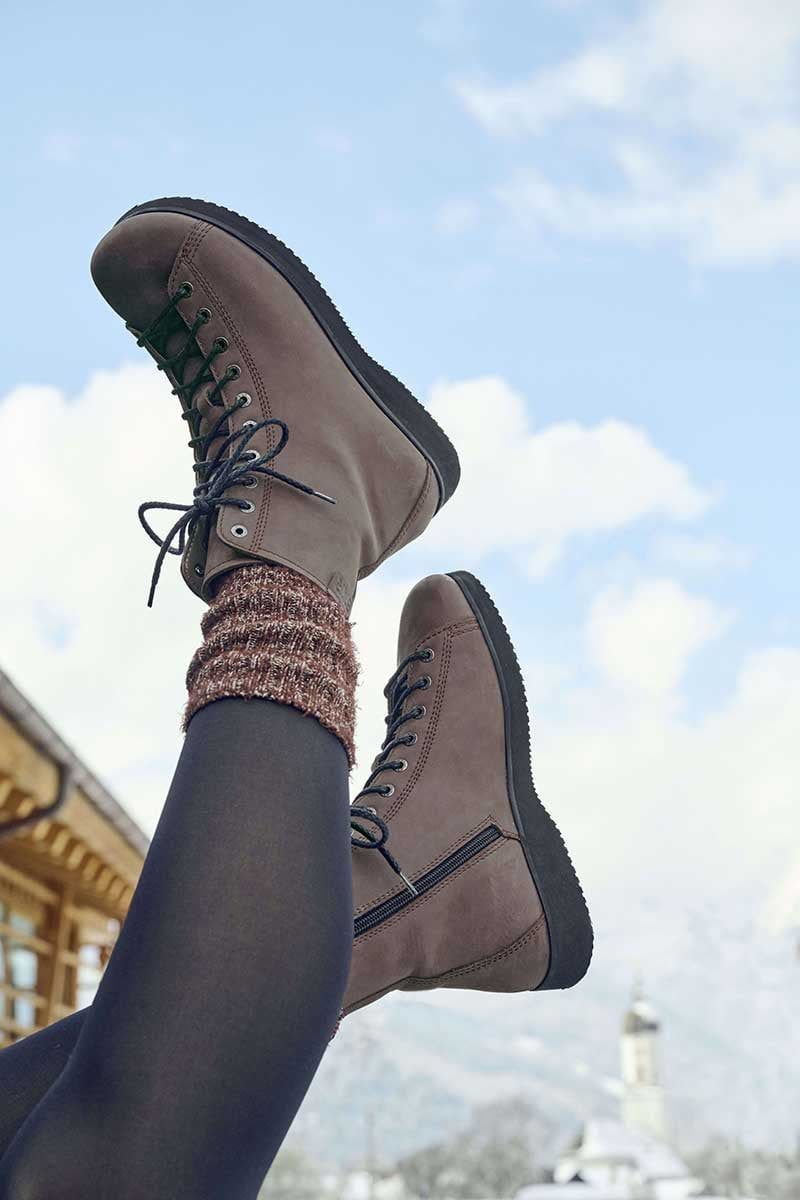 Braune Stiefeletten mit Schnürung, Reißverschluss und flacher Sohle. Bein mit Socken und Strumpfhose.