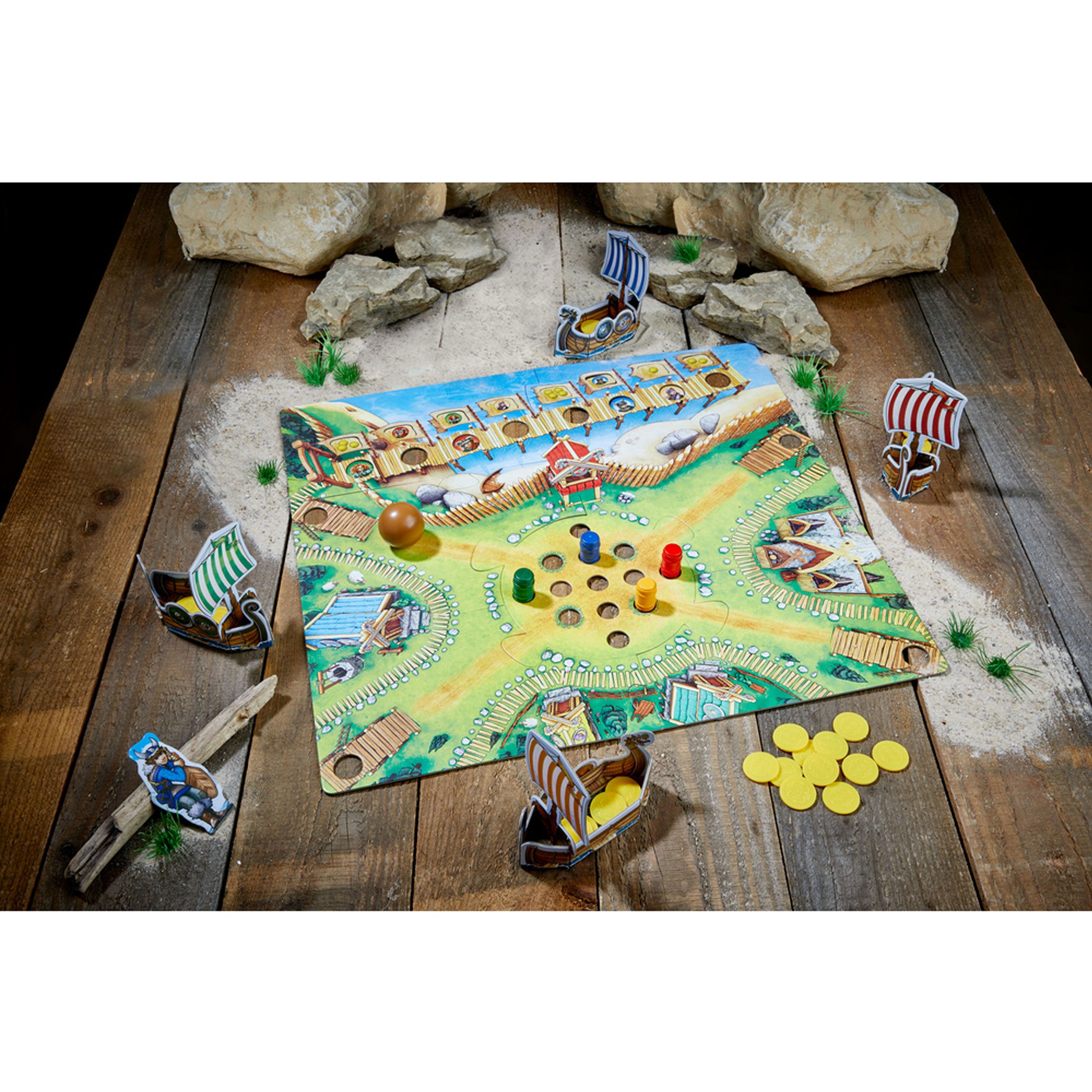 Spielbrett mit Wikingerschiffen, Holzstücken und gelben Münzen. Auf Holzuntergrund mit Sand und Steinen dekoriert.