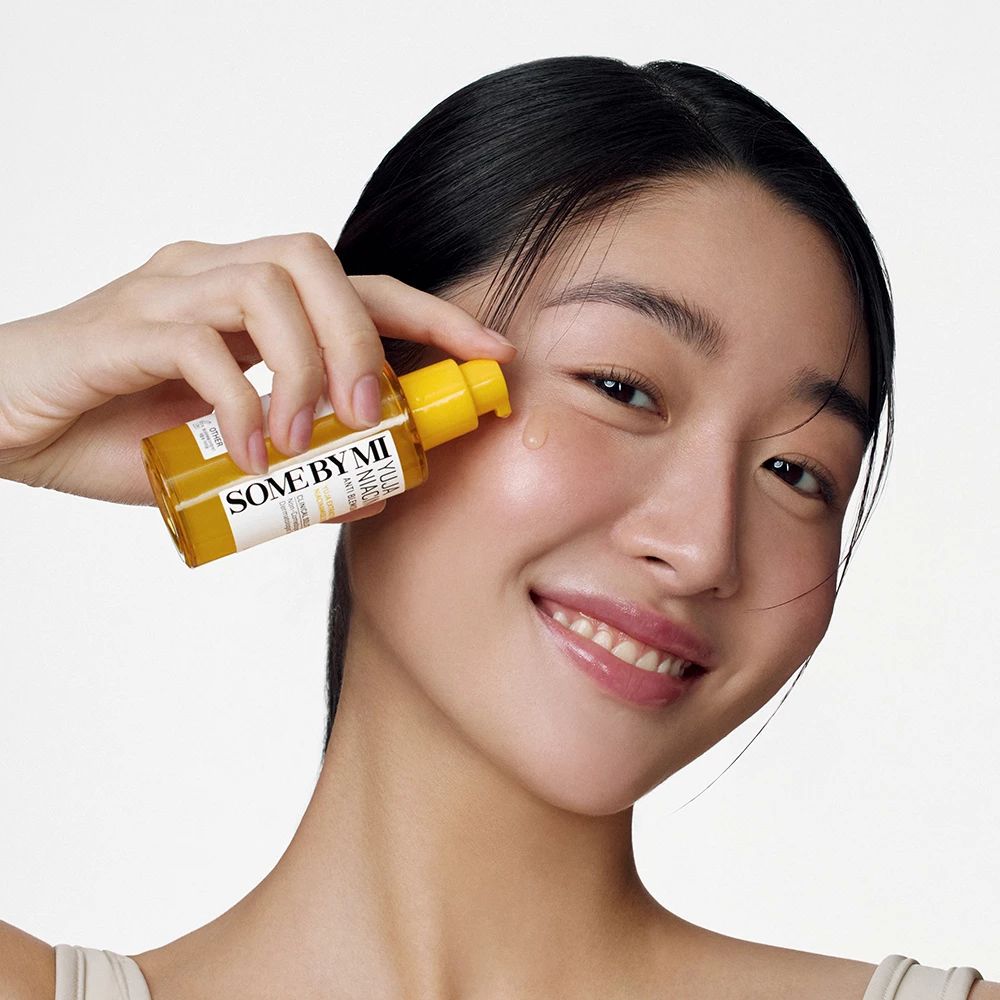 Asiatische Frau trägt Serum auf. Flasche mit Aufschrift SOME BY MI Yuja Niacin.