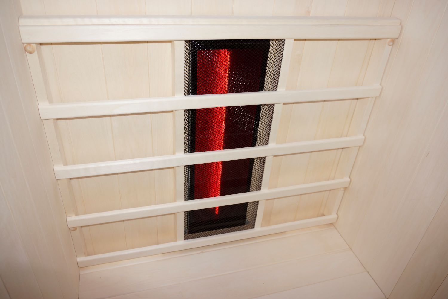 Innenansicht der Infrarotsauna. Roter Infrarotstrahler hinter einem schwarzen Gitter. Holzrahmen und -elemente.