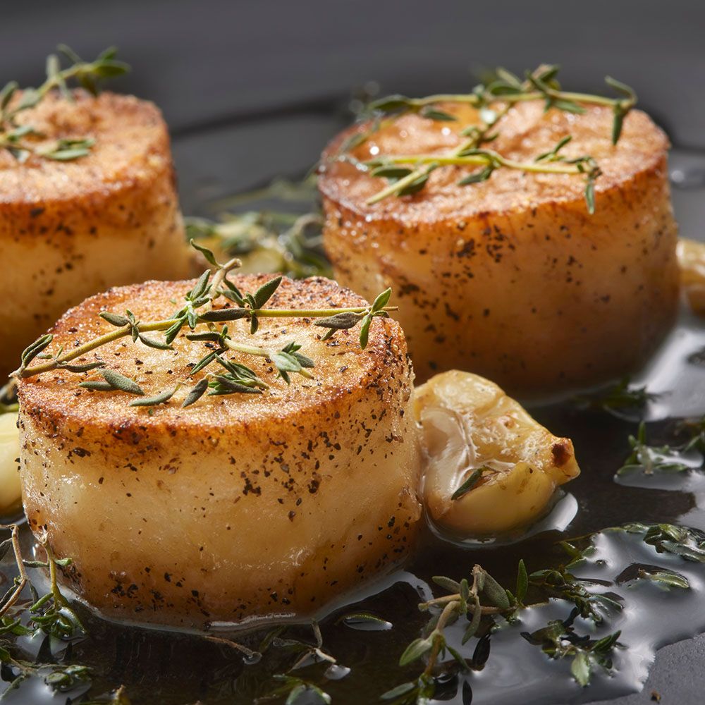 Drei gebratene Jakobsmuscheln. Mit Kräutern und Knoblauch in einer dunklen Flüssigkeit. Nahaufnahme.