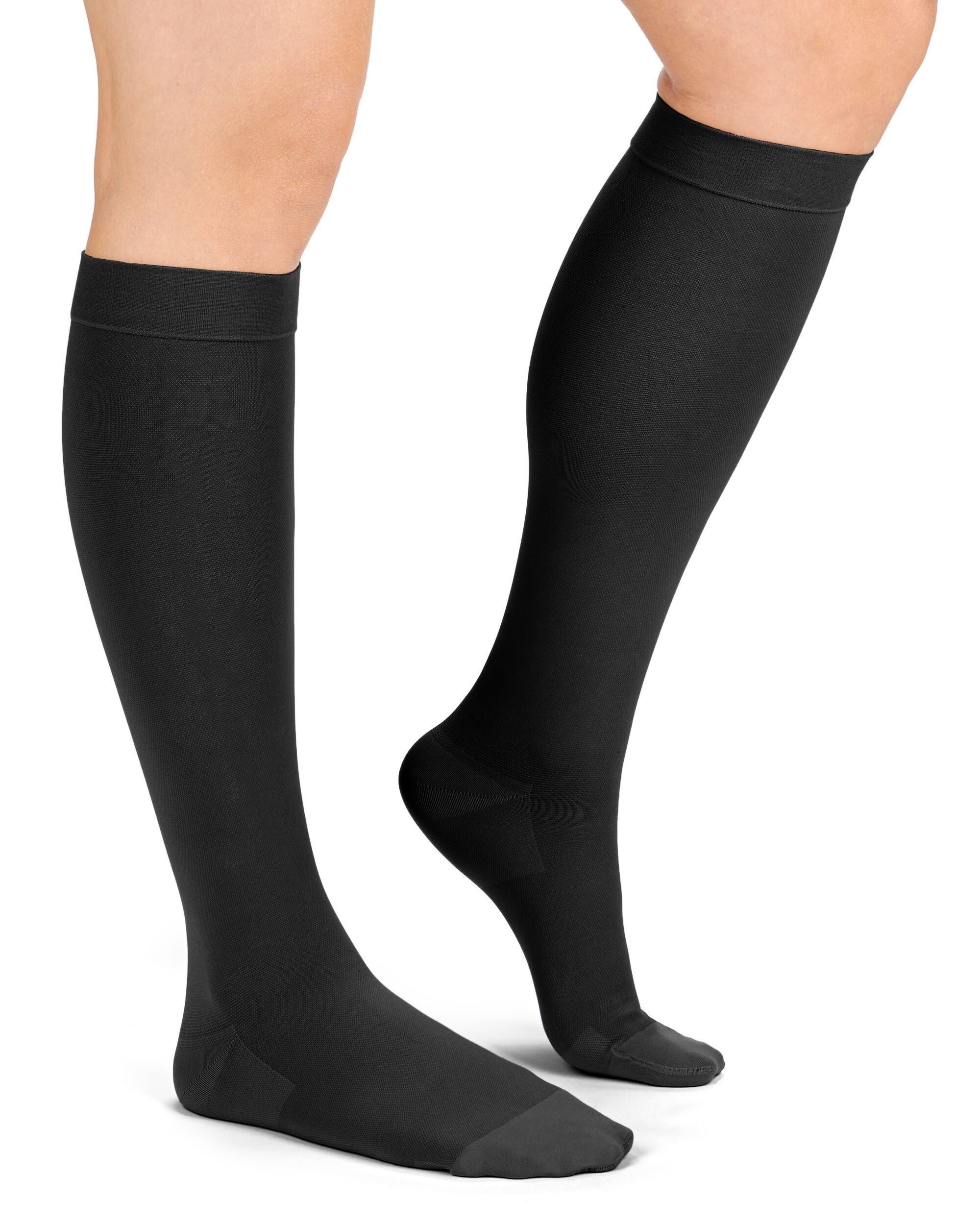 Zwei Beine mit schwarzen Kompressions-Kniestrümpfen. Blick von vorne, Füße auf dem Boden.