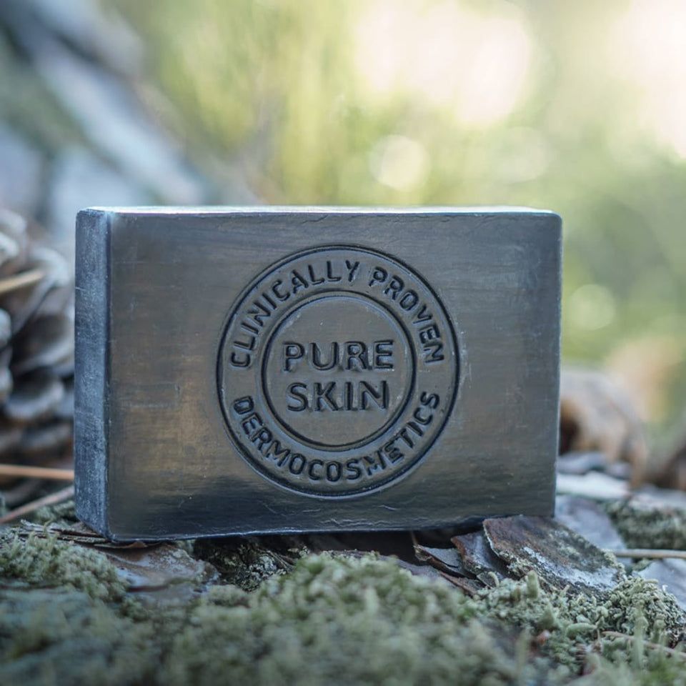 Rechteckige schwarze Seife mit Prägung. Auf Moos und Kiefernnadeln. Text: Clinically Proven, Pure Skin.