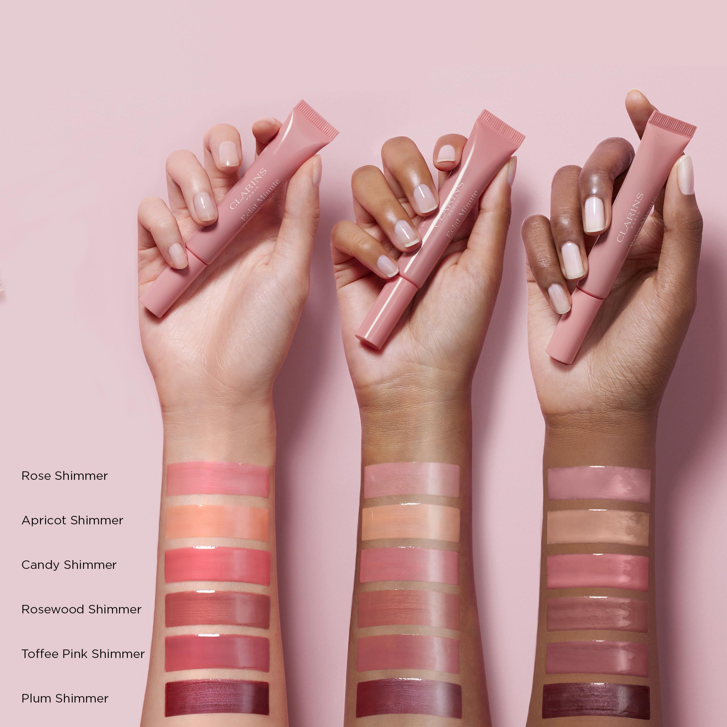 Hände mit Farbmustern von Clarins Lip Perfector. Verschiedene Farbtöne aufgetragen. Rosa Hintergrund.