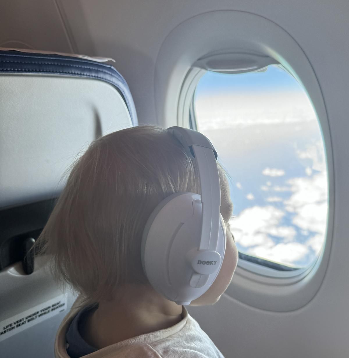 Kind im Flugzeug mit grau-weißem Gehörschutz. Blick aus dem Fenster.